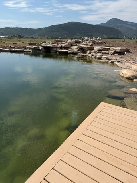 Pond construction with stone edging, a rock waterfall and a deck beside the water